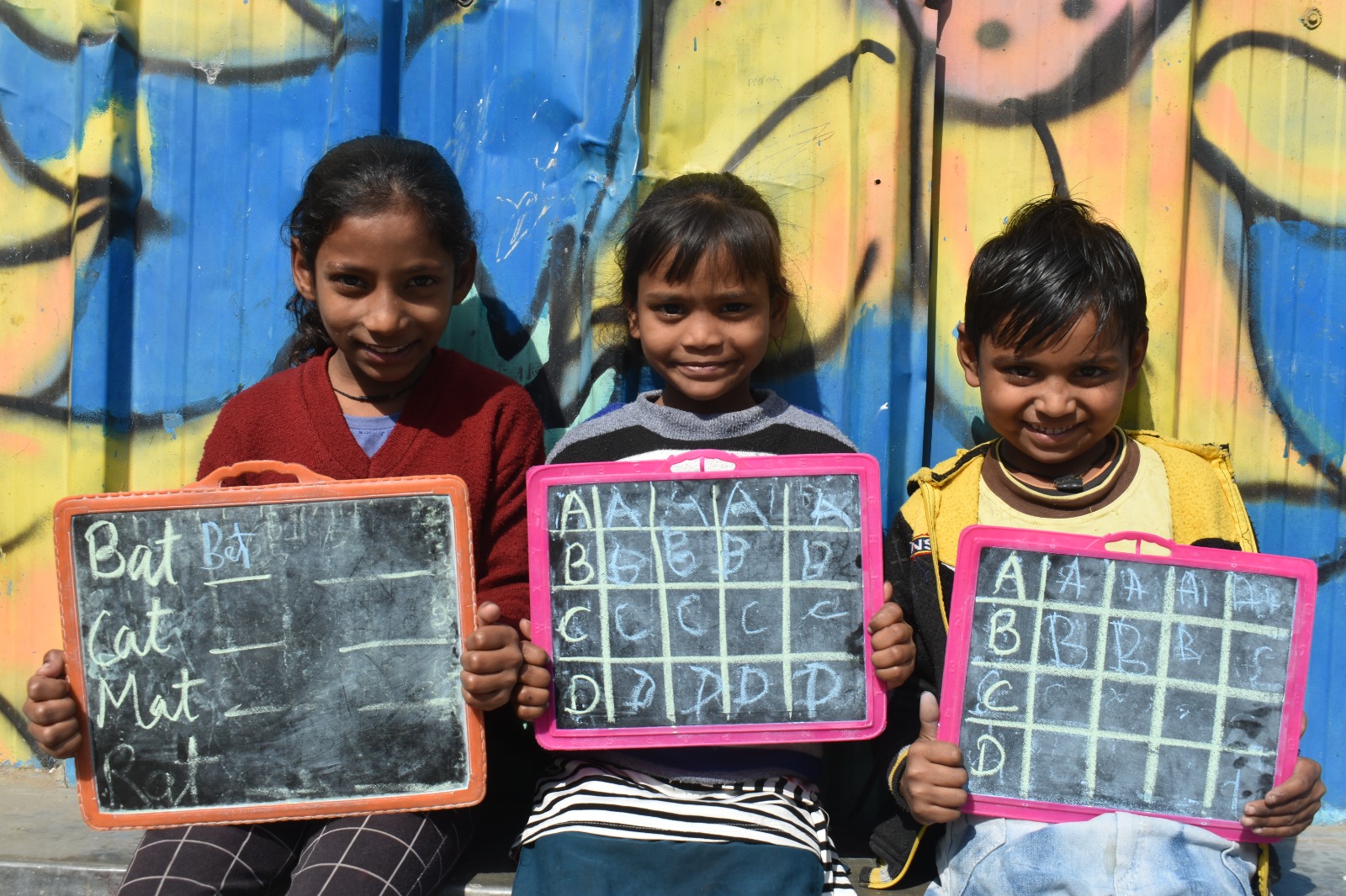 3 underprivileged children holding chalkboard